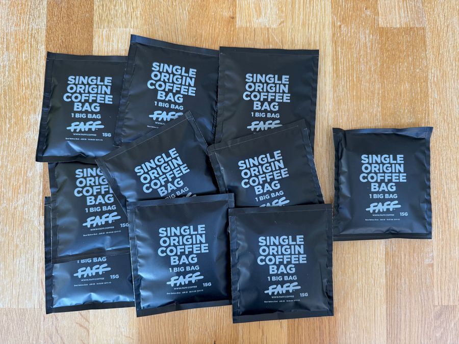 A photo showing ten black packets labeled “Single Origin Coffee Bag” with “1 Big Bag” and “FAFF” branding, each containing 15g of coffee, arranged on a wooden surface.